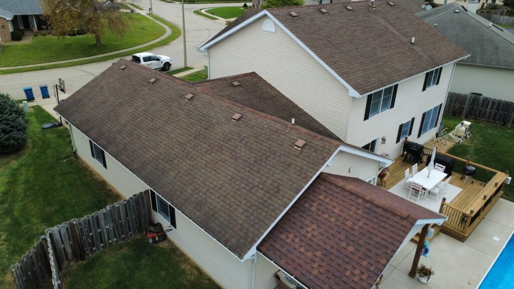 Worn brown asphalt shingle roof on a two-story Springfield, IL home before replacement, seen from the back over the deck and pool