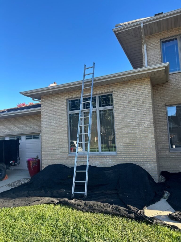 Ladder and protective tarps set up beside a tan brick Springfield, IL home before roof tear-off
